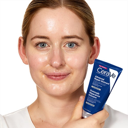 Woman holding up CeraVe Advanced Repair Ointment after applying it to the face protect the skin barrier
